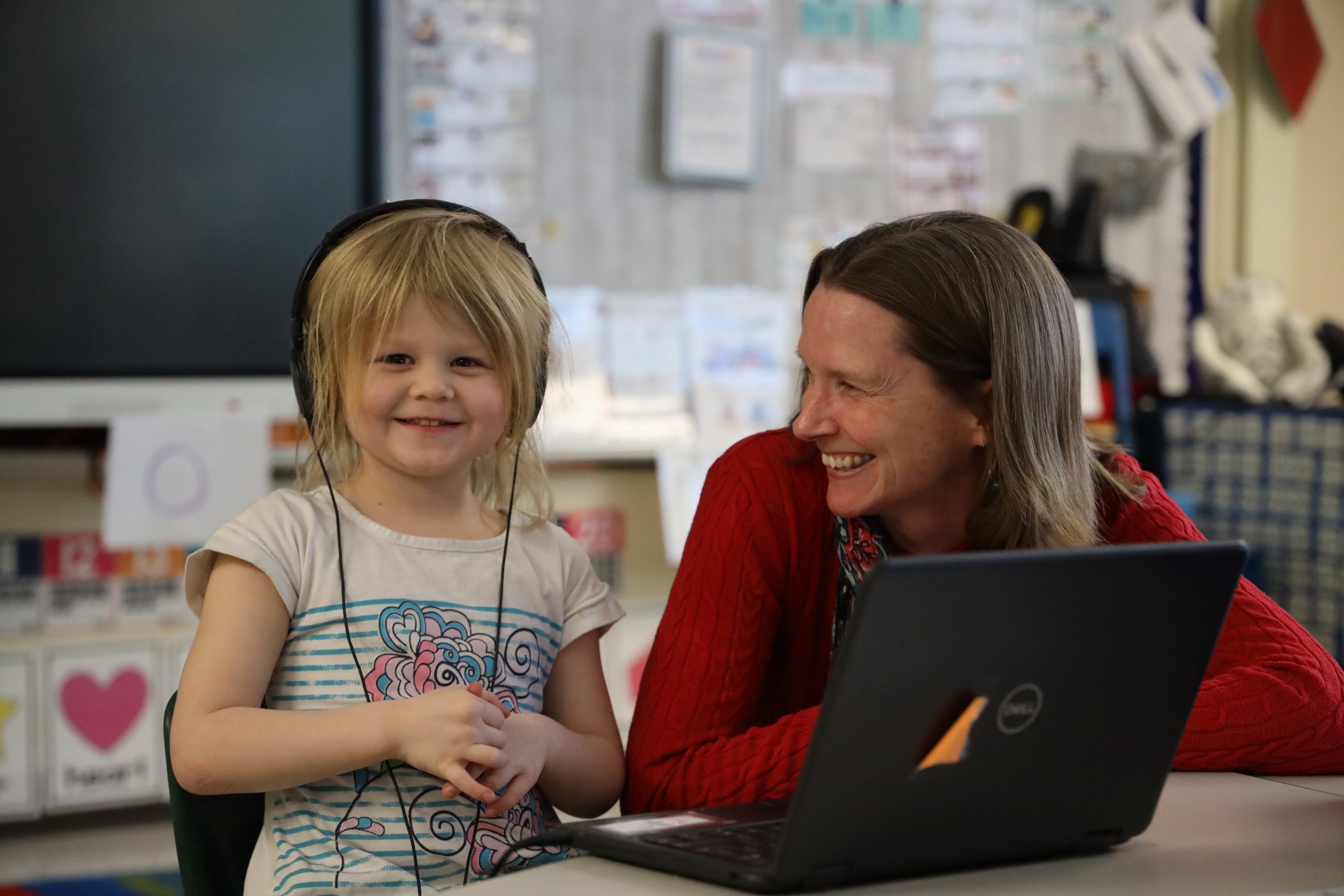 Child with headphones on is next to school principal. They are both smiling.