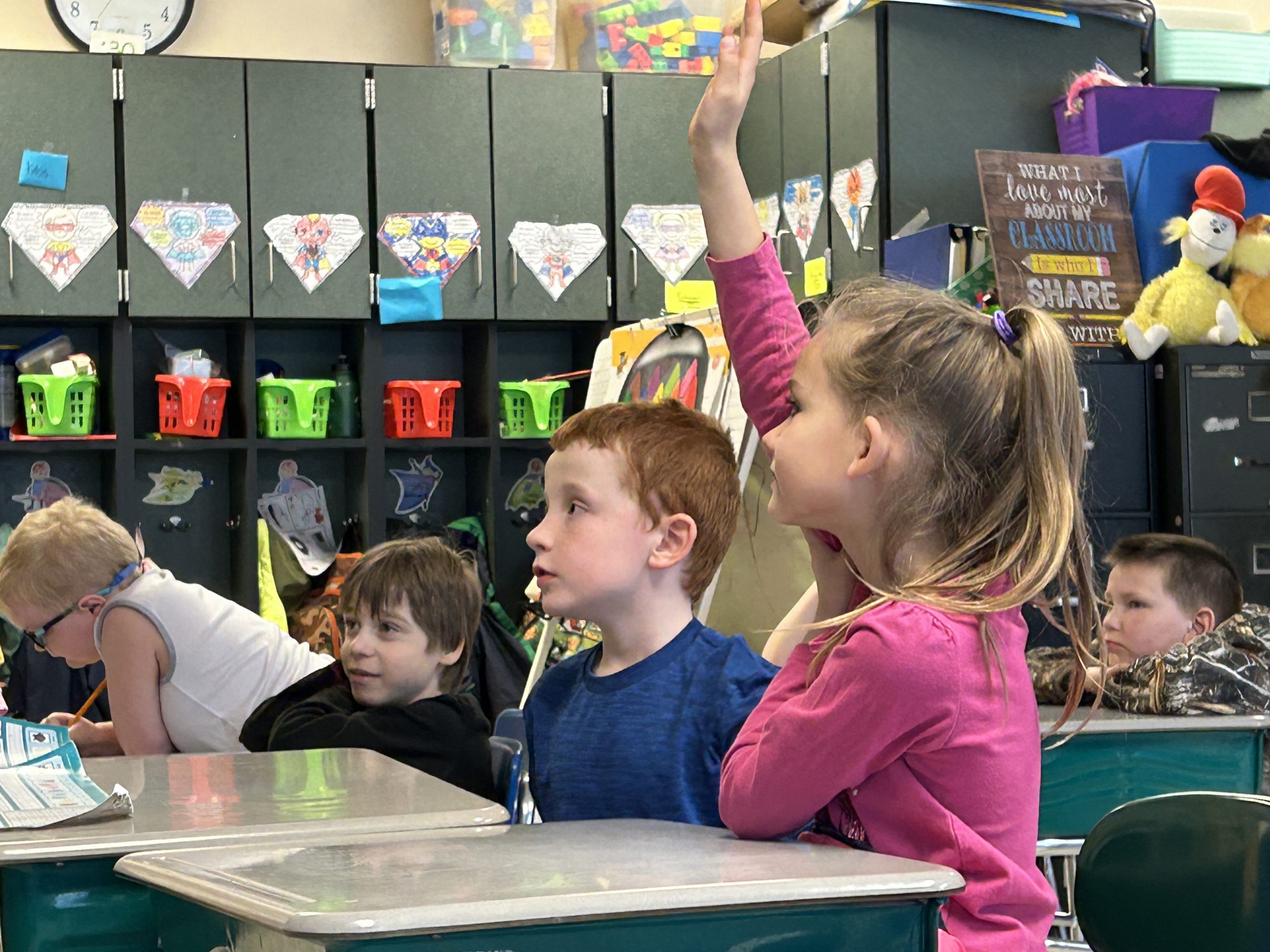 Grade school students in classroom. A girl is raising her hand.