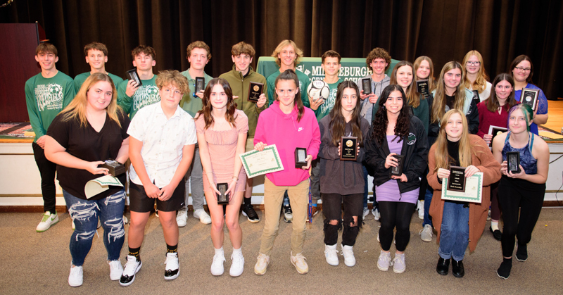 Student-athletes stand in a group, holding awards.