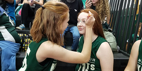 a student paints another student's face at the pep rally