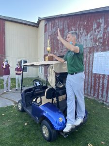 MCS Golf Coach holding a trophy and standing on the golf cart at the Western Athletics Conference Golf Championship