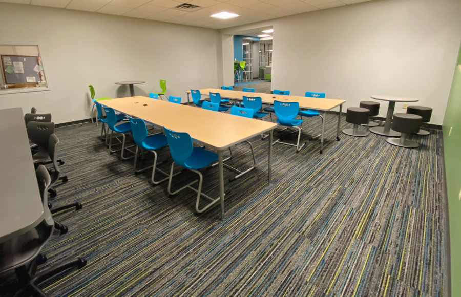 room off of library with different tables and chairs and window to tech department assistance