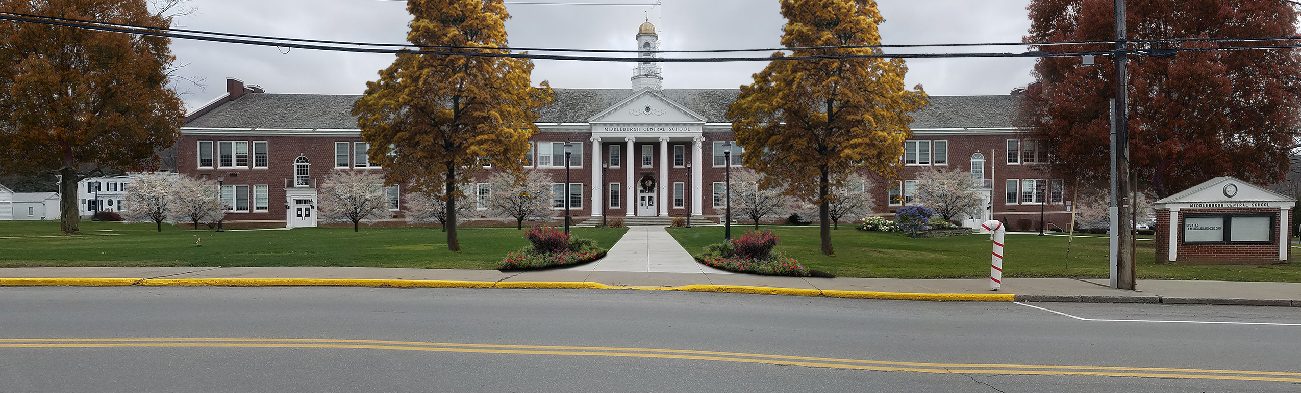 front courtyard of high school with two trees near the road and flower beds