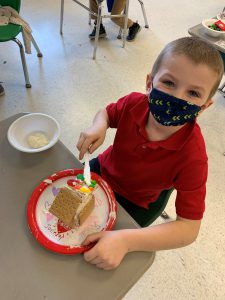 student looks up from spreading icing on gingerbread house 