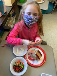 student holds pieces of candy in hand as she makes gingercread house