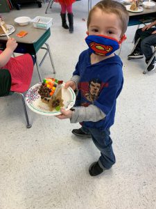 student holding decorative gingerbread house he made