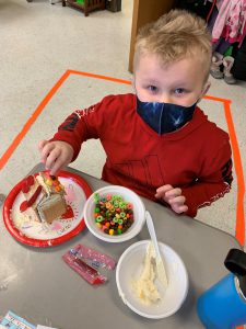 student places candy on gingerbread house