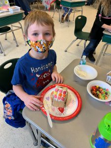 student looks up for picture while making gingerbread house