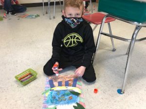 student holding glue is pasting layers on his fish bowl drawing