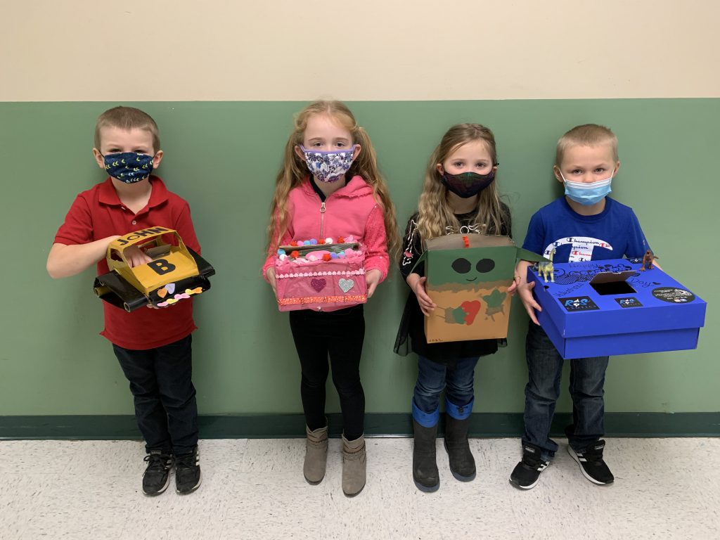 four students standing side by side holding valentine's boxes they made