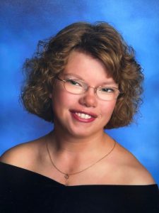 senior picture of student with glasses and a nice smile, wearing black drape with a blue background