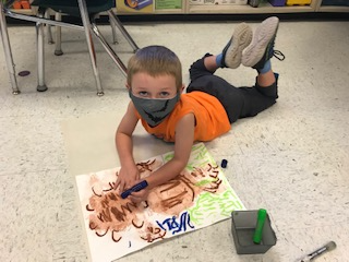 kindergarten student laying on the floor painting a teddy bear