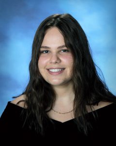 senior picture of a girl wearing a black drape with long black hair split down the middle and a big smile with white teeth.