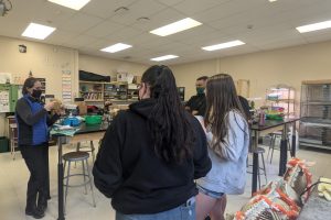 Vet shows surgical tools to agriculture students. Four students stand in a circle watching her demonstration.