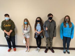 five students wearing face masks stand along a wall for a picture