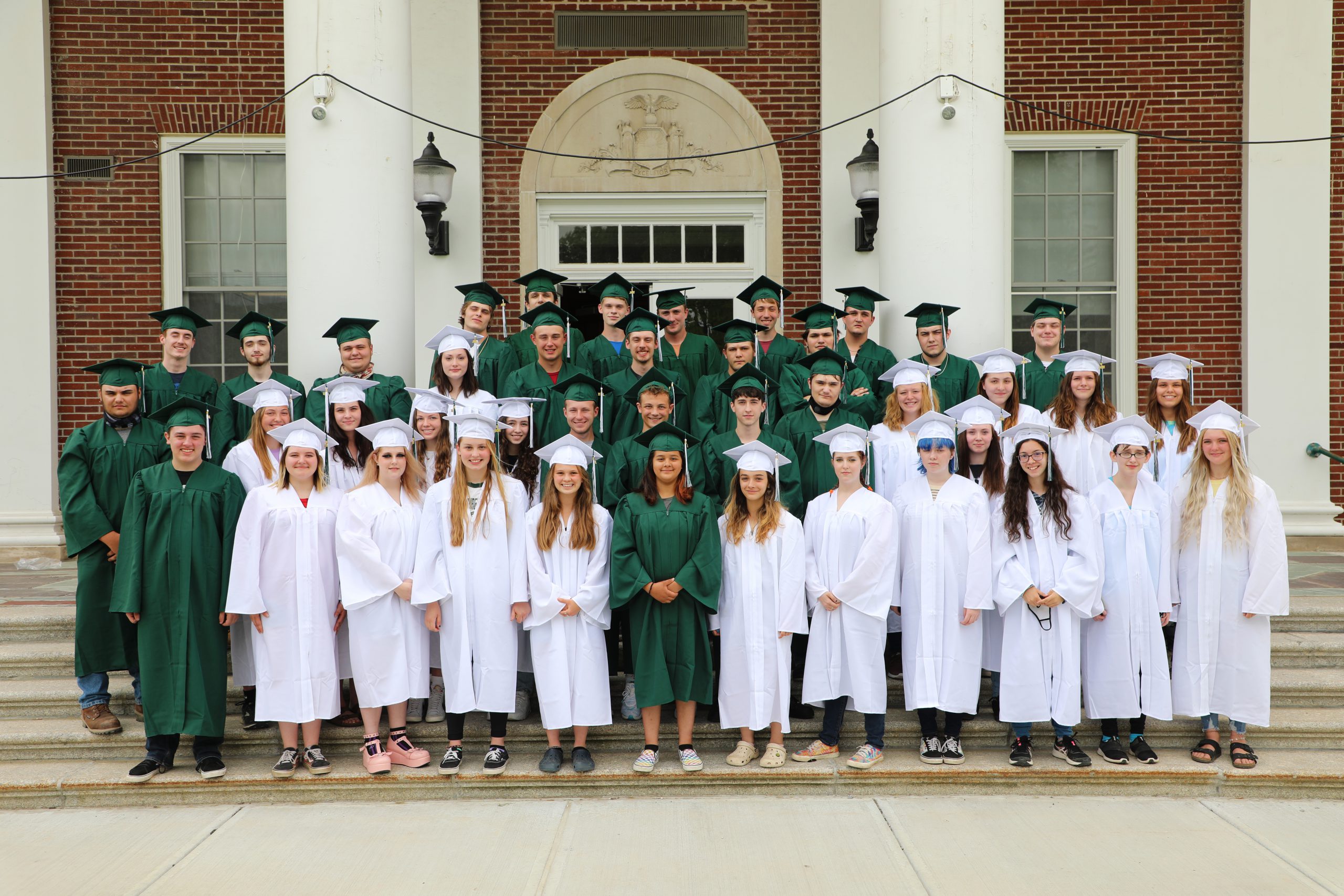 seniors stand together in their caps and gowns in front of the high school