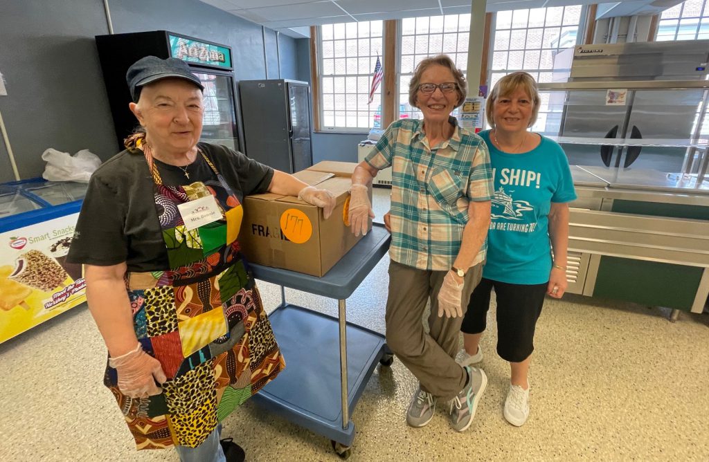 three women volunteers standing in the cafeteria near a box