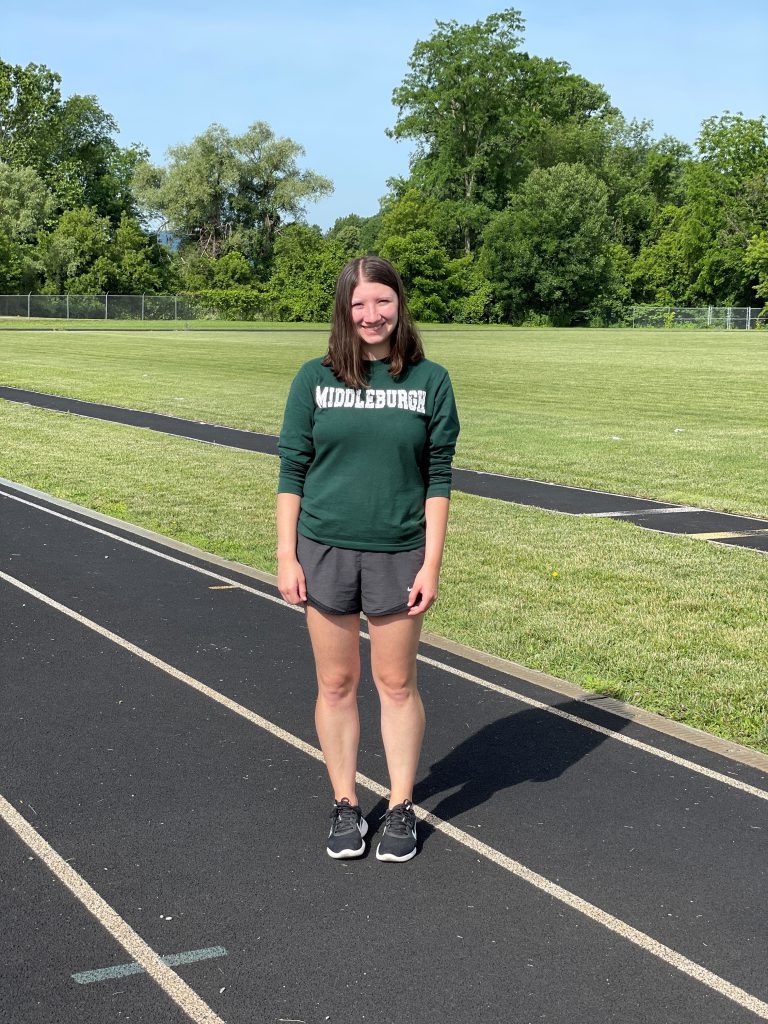 substitute teacher stands on track wearing a Middleburgh T-shirt