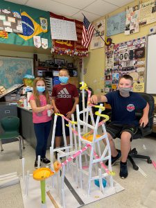 three studentsstanding behind a paper roller coaster they made