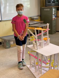 student standing proudly next to a paper roller coaster she created in her classroom