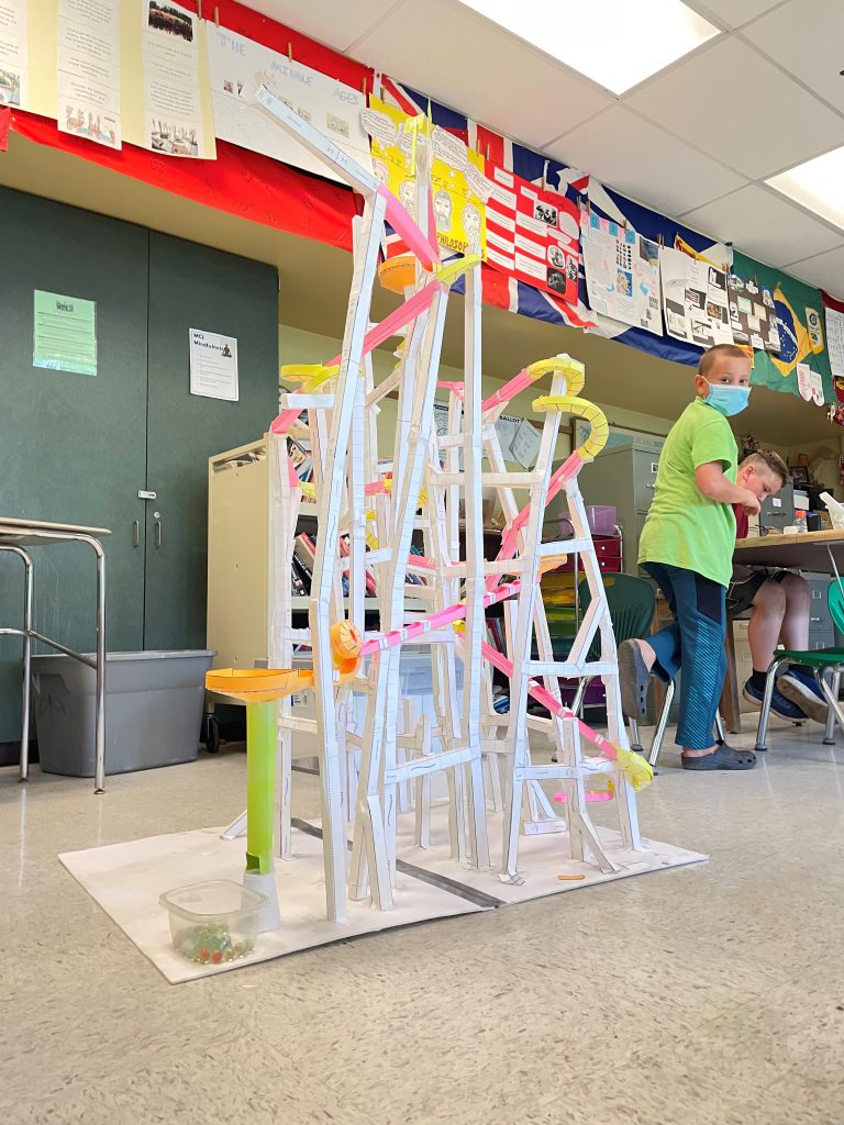 tall paper roller coaster and boy looking back at his creation