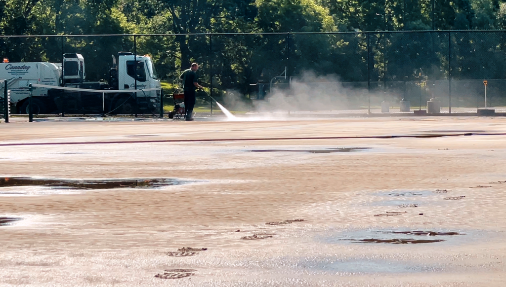 man using pressure hose to clean tennis court