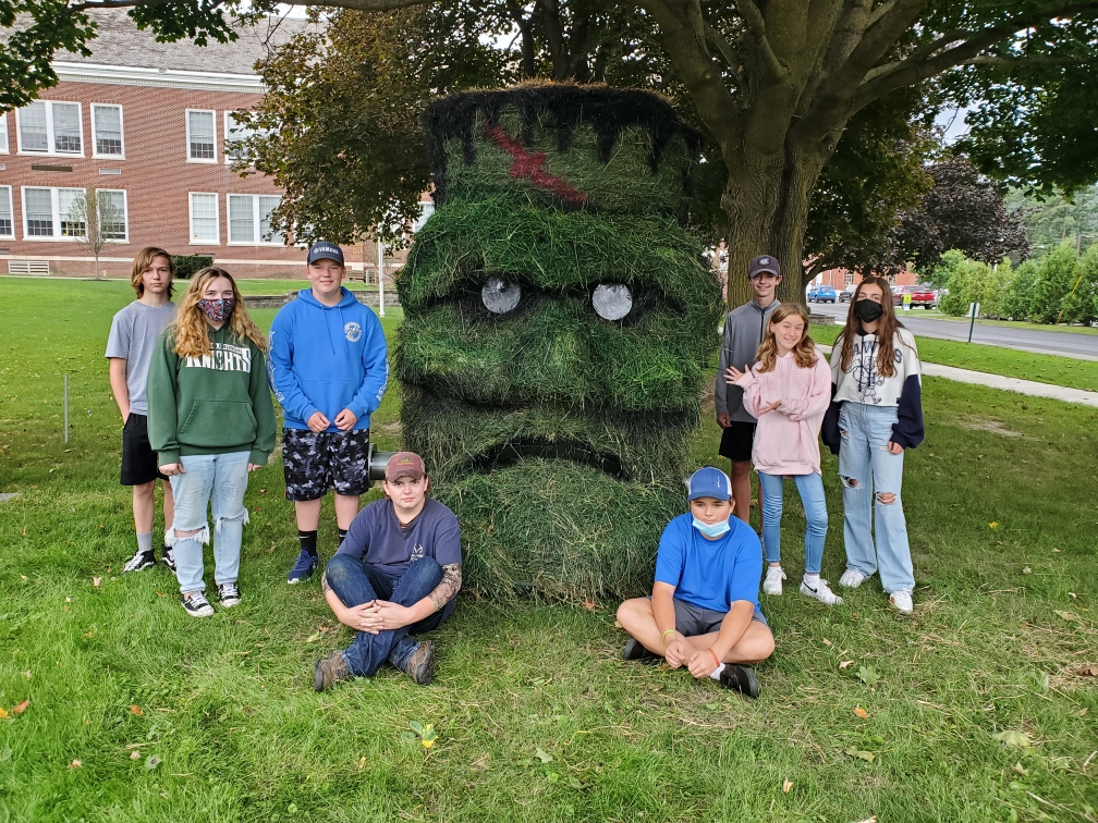 eight students standing around a huge Frankenstein head made out of grass