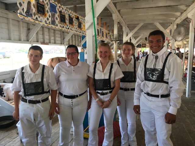 five FFA students, all wearing white, standing in a barn at a fair