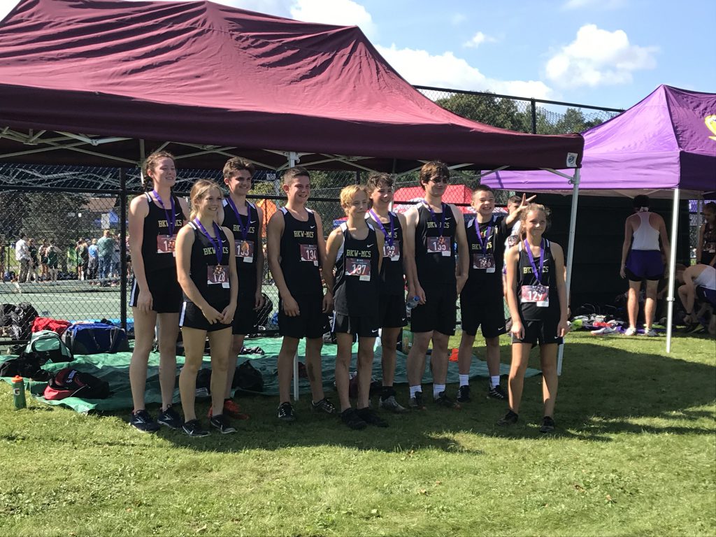 ten students in cross country outfits standing outside wearing medals