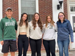 five seniors stand outside on the high school steps with their arms around each other