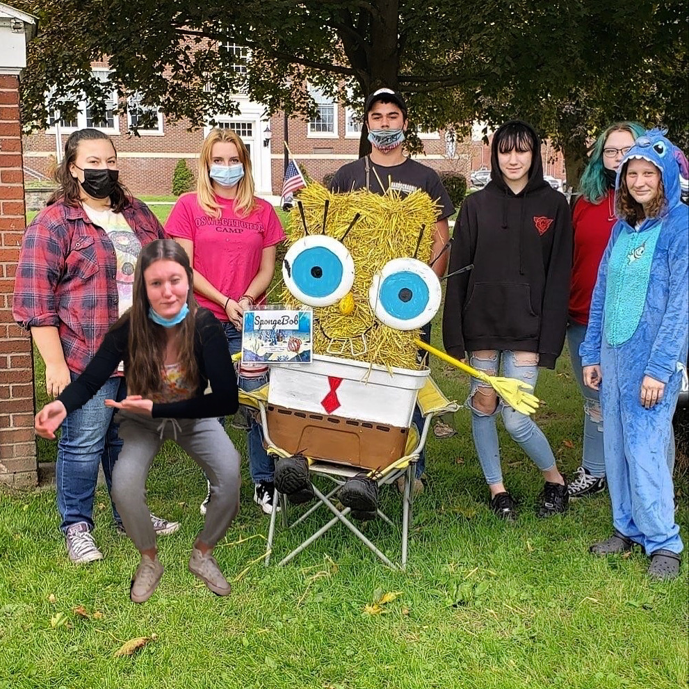 seven students standing around a SpongeBob scarecrow sitting on a chair