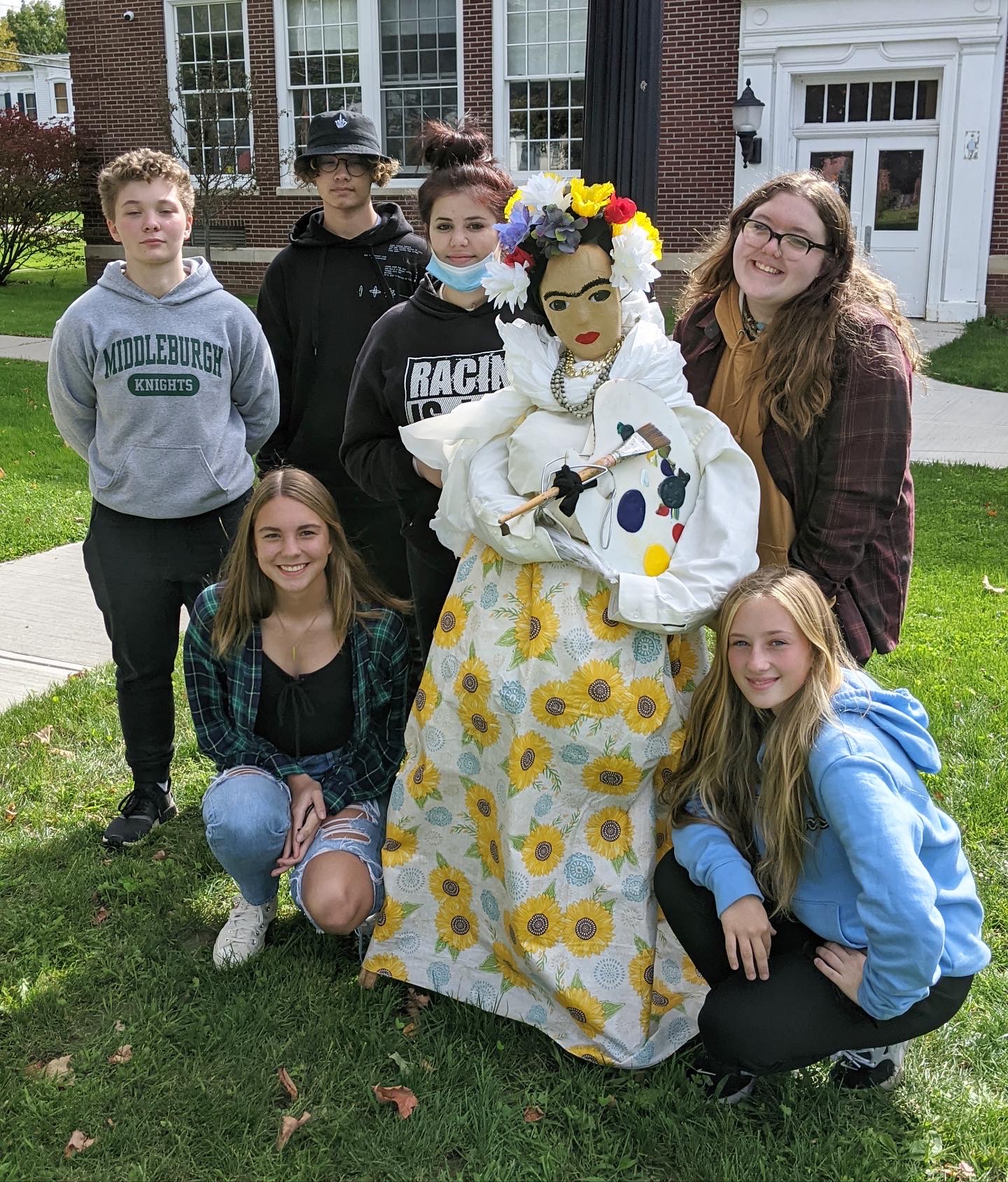 six students standing around a scarecrow they made of Frida