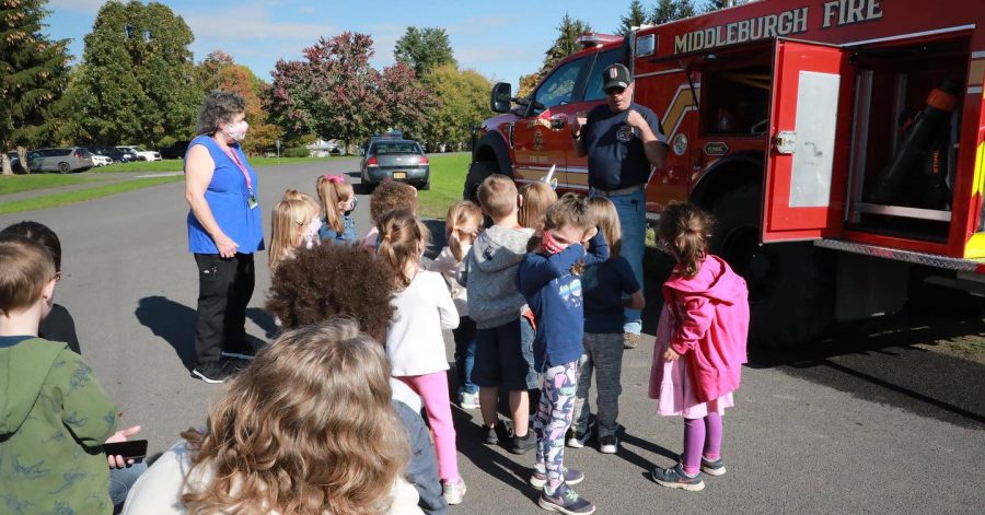 students gathered around a firetruck and a firefighter talking to them about safety