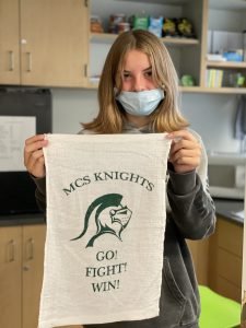 student with shoulder length blonde hair holds up spirit towel at the school store