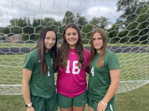 three soccer players standing together in uniform outside in front of a goal