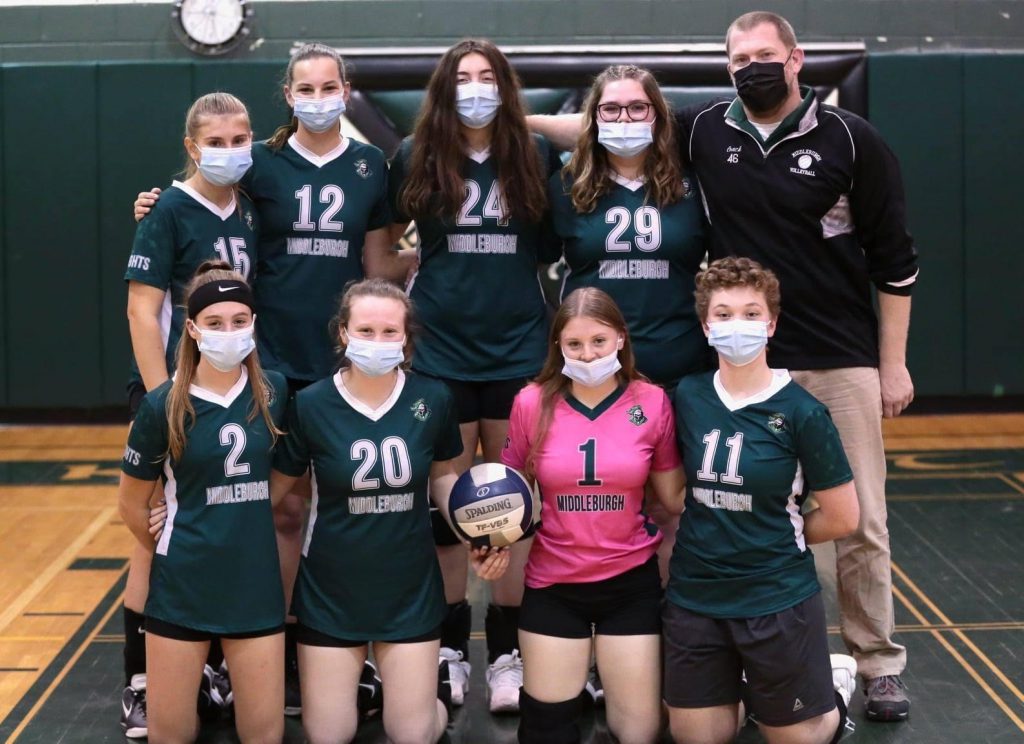volleyball players standing with their uniforms and face masks on and their coach is standing beside them