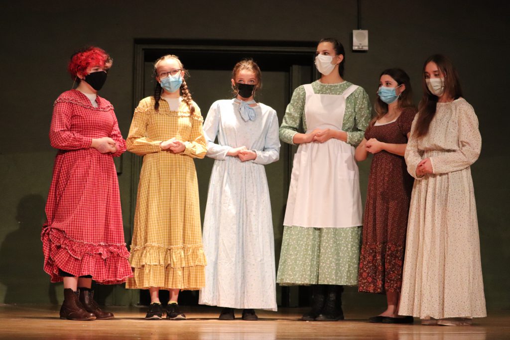 six female actors in long dresses on stage