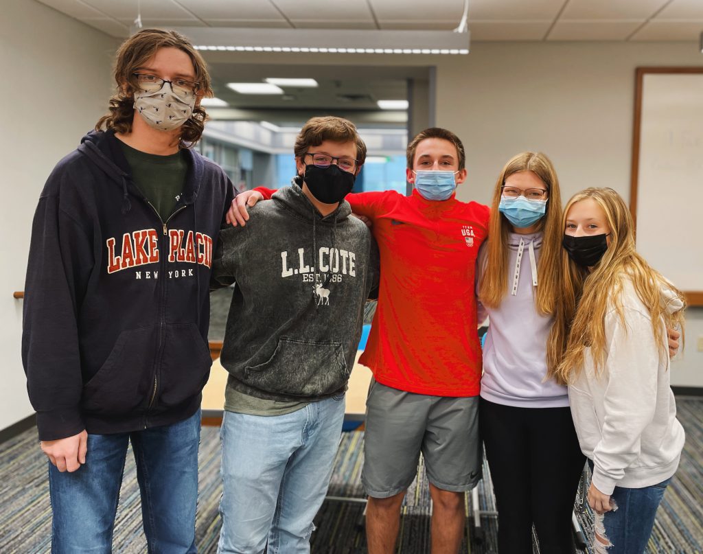 five students standing in order of tallness wearing face masks and their arms are around each other 