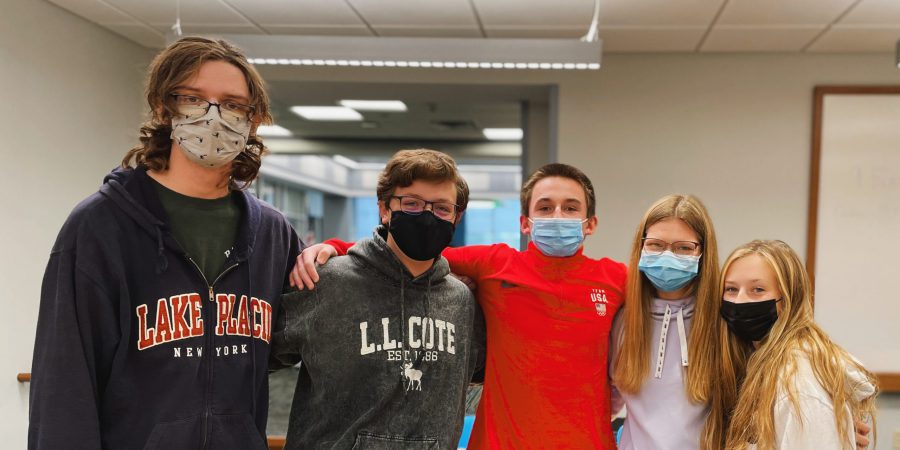 five students standing in order of tallness wearing face masks and their arms are around each other