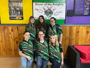 three students wearing green bowling shirts stand and three other bowlers kneel in front of them