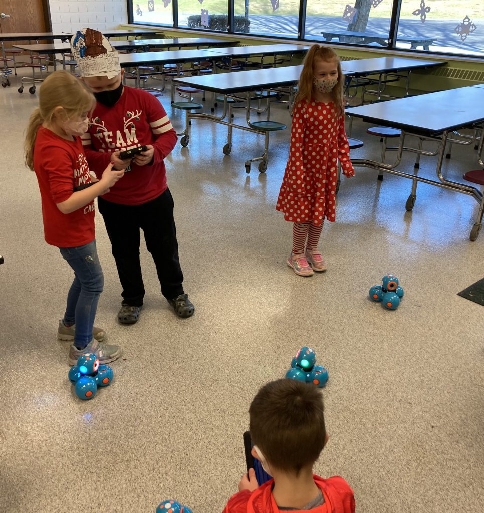 four students with remote controls in their hand and robots on the ground