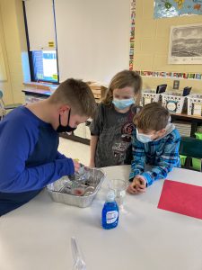 three students leaning over a project to make a volcano