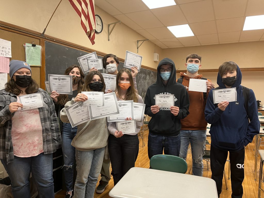 eoght students stand next to each other holding certificates