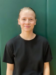 student dressed on black standing in front of a green backdrop with her hair pulled back and smiling