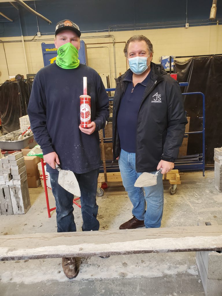 students with tools in his hand standing next to business owner after laying brick