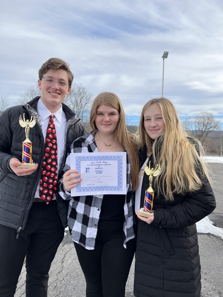 three students standing together in a line. The first person is holding a trophy, the second person is holding a certificate, and teh third person is holding a trophy