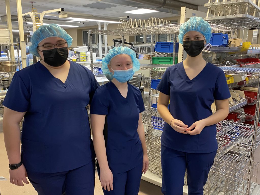 three students in medical scrubs and caps on their head are standing inside a medical lab