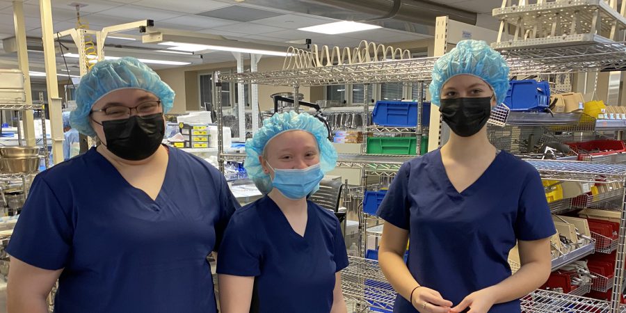 three students in medical scrubs and caps on their head are standing inside a medical lab