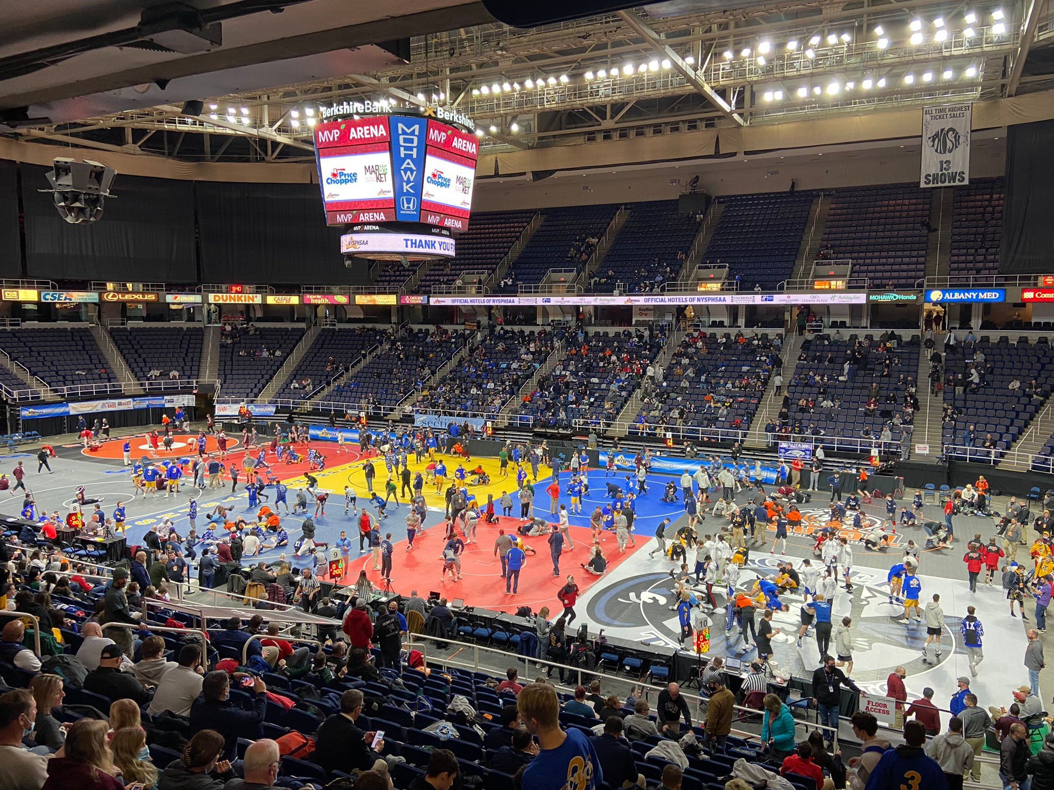 huge arena with spectators in bleachers and wrestlers standing around on the court