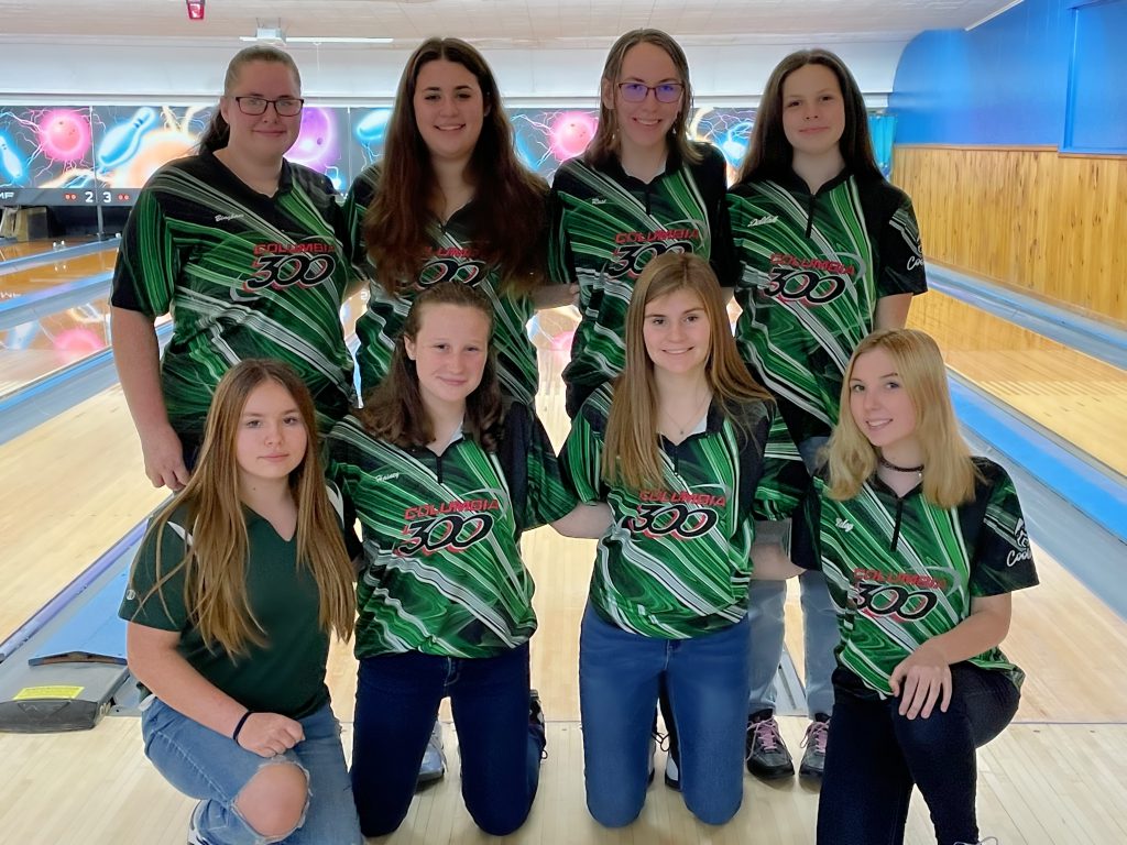 girls bowling team wearing green, black, and white shirts posing together for a picture at the bowling alley